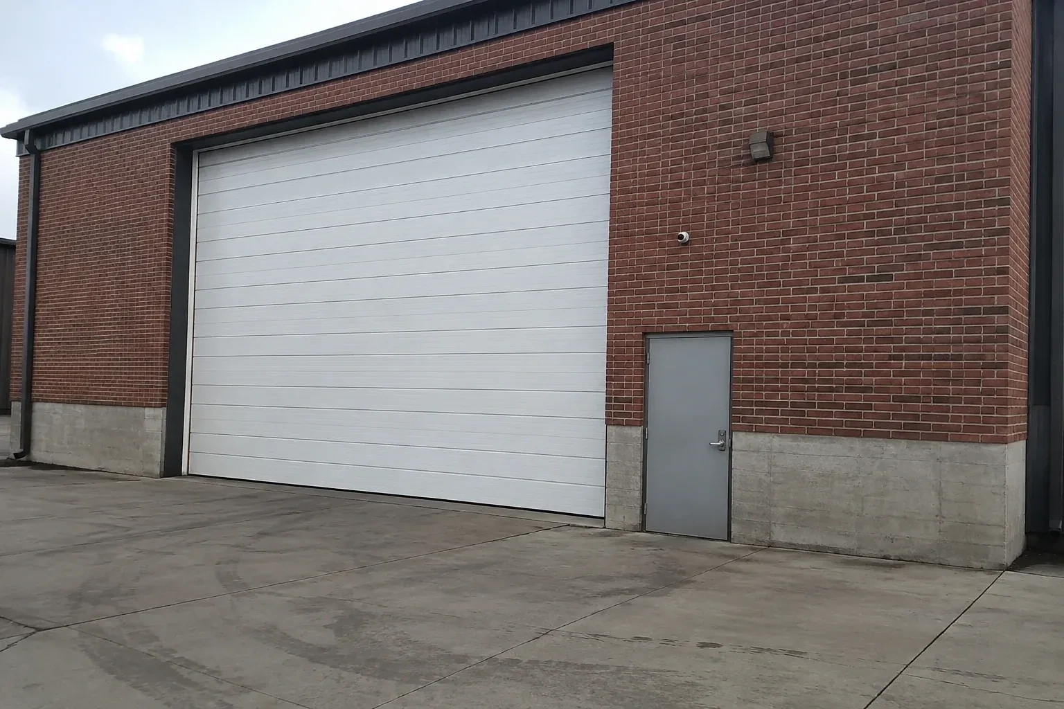 Tall closed sectional loading door beside a personnel door at a brick unit. — Commercial Sectional Door Repair, Mississauga