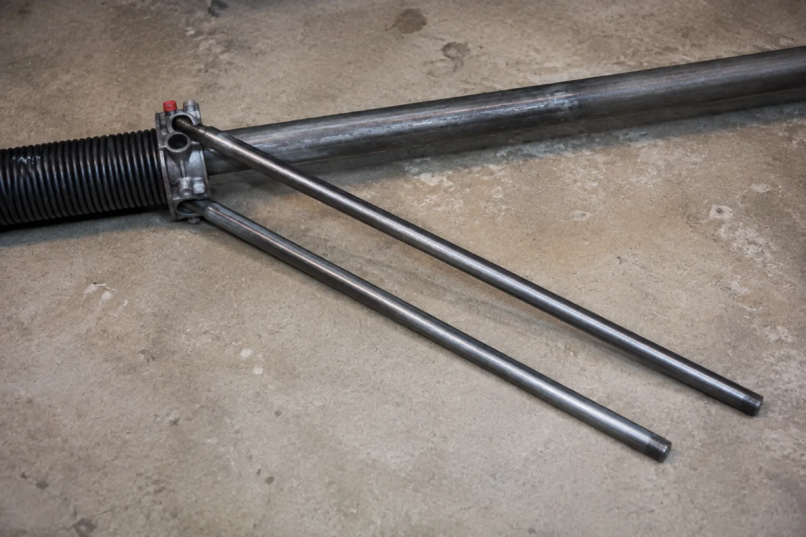 Two long steel winding bars inserted into the cone of a black torsion spring lying on a concrete floor. — Streetsville